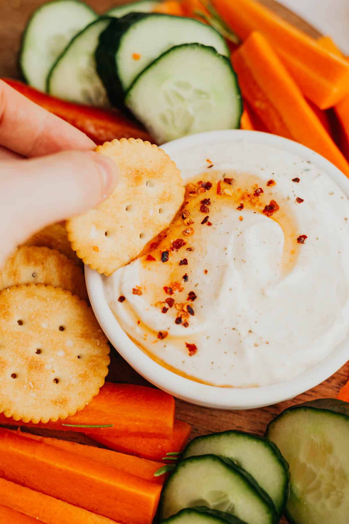 A hand holding a cracker, dipping into a whipped ricotta dip.