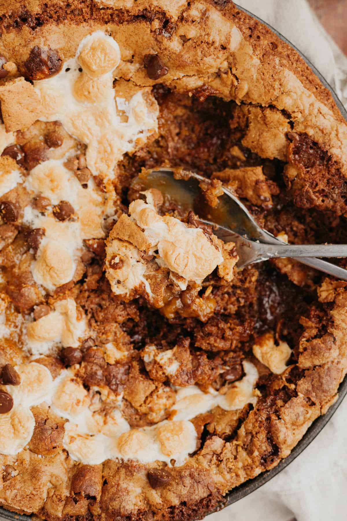 A close up of a marshmallow cookie skillet, there is a spoon scooping out some of the cookie.