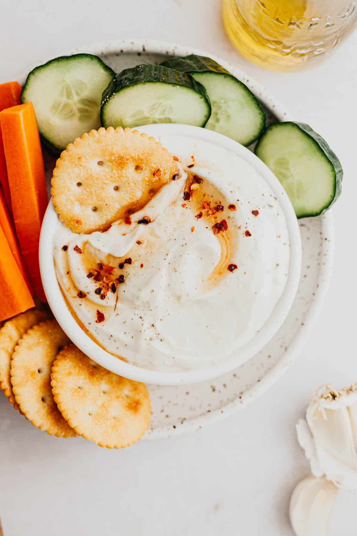 A white bowl filled with whipped ricotta dip and drizzled with hot honey, it is surrounded by cut up vegetables.