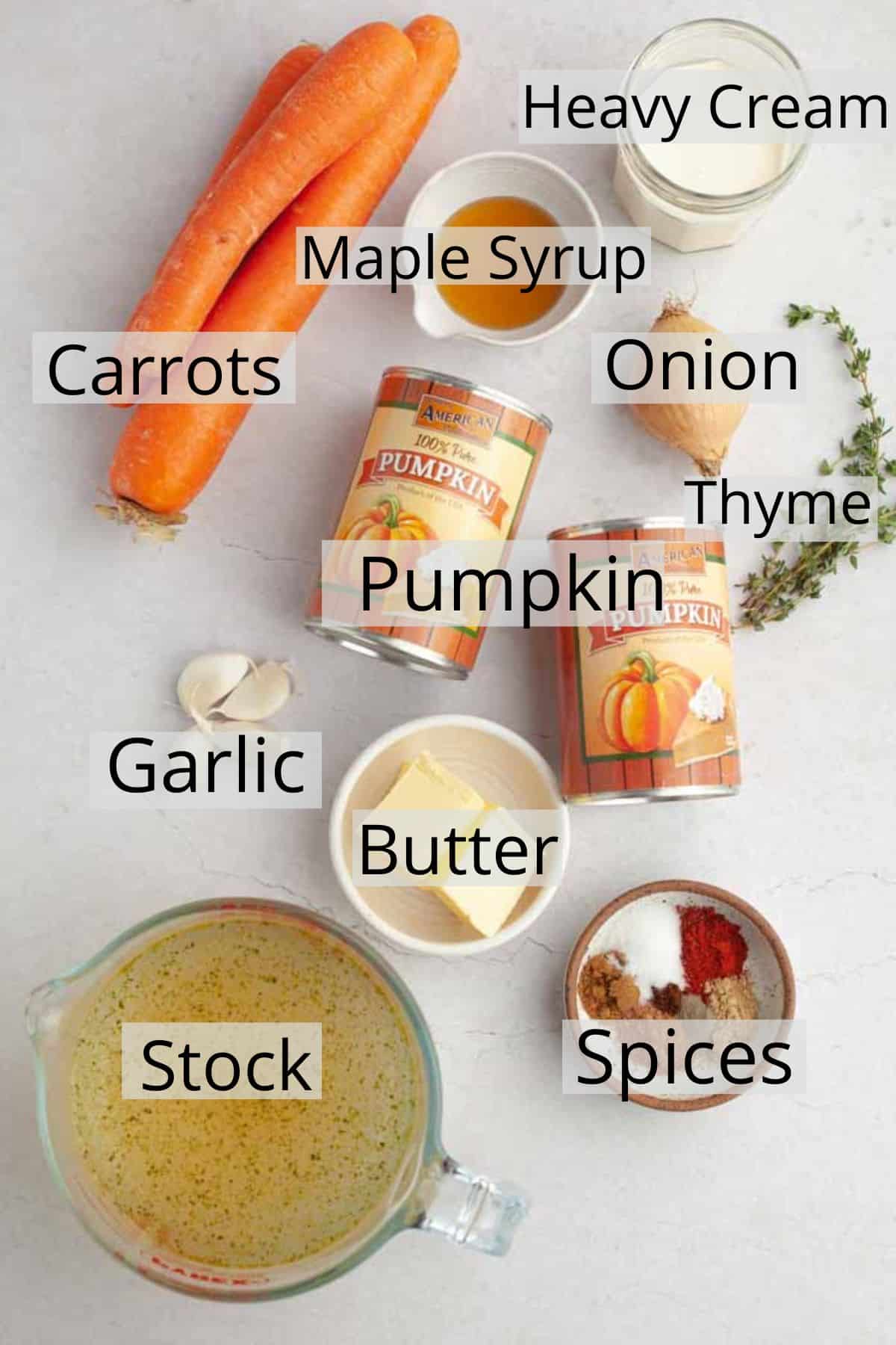 All the ingredients needed for pumpkin carrot soup on a white marble counter.