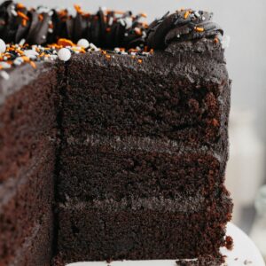 A three layer black velvet cake, sliced on a white cake stand.