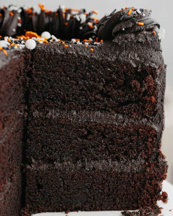 A three layer black velvet cake, sliced on a white cake stand.