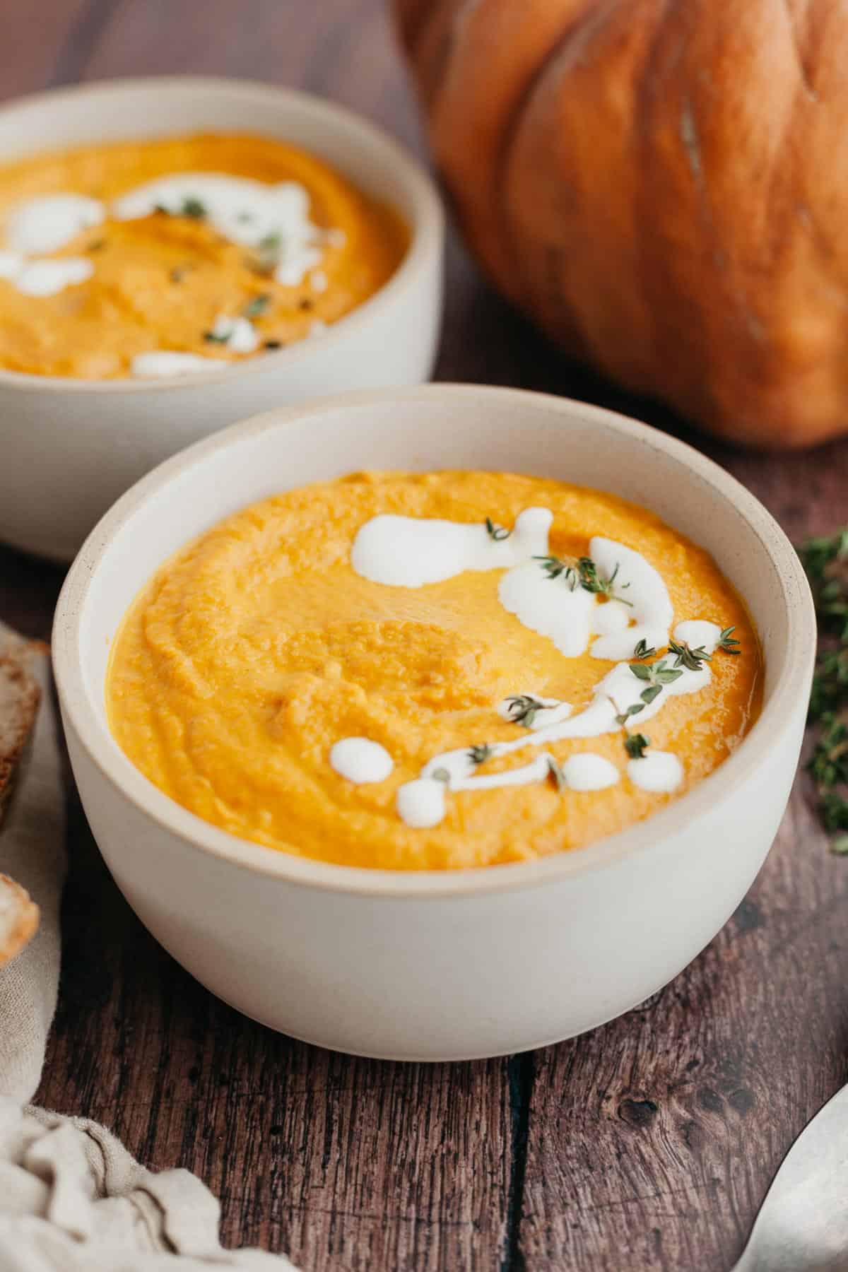 A white bowl with pumpkin carrot soup in it, drizzled with heavy cream and thyme.