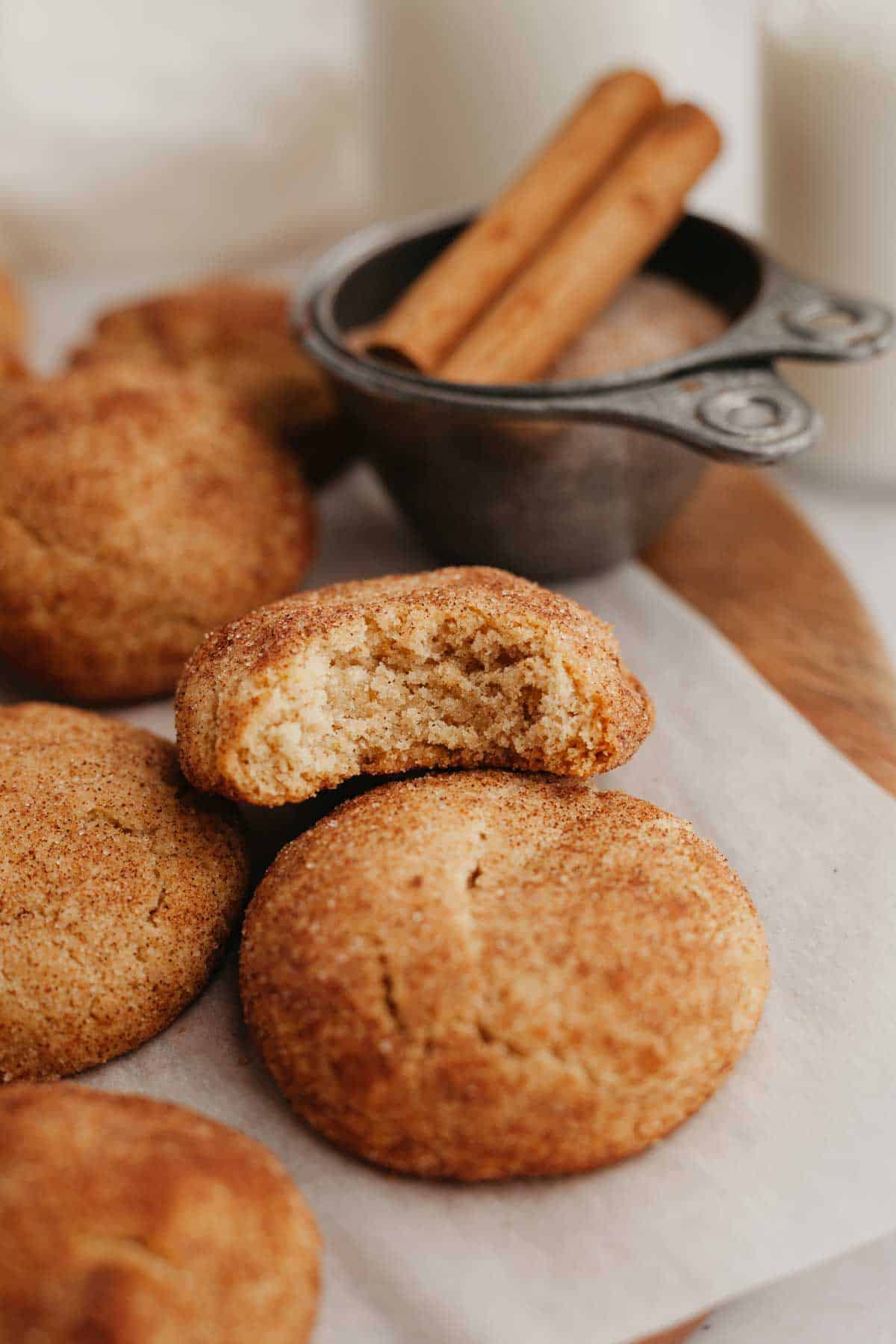 Several snickerdoodles on parchment paper, one has a bite taken out of it.
