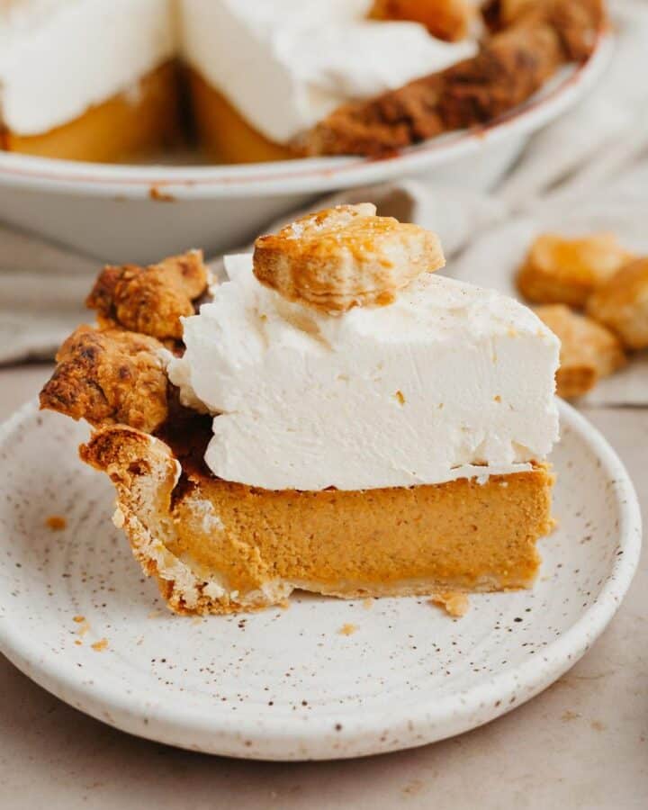 a slice of pumpkin pie on a small plate, the pie is covered in whipped cream.