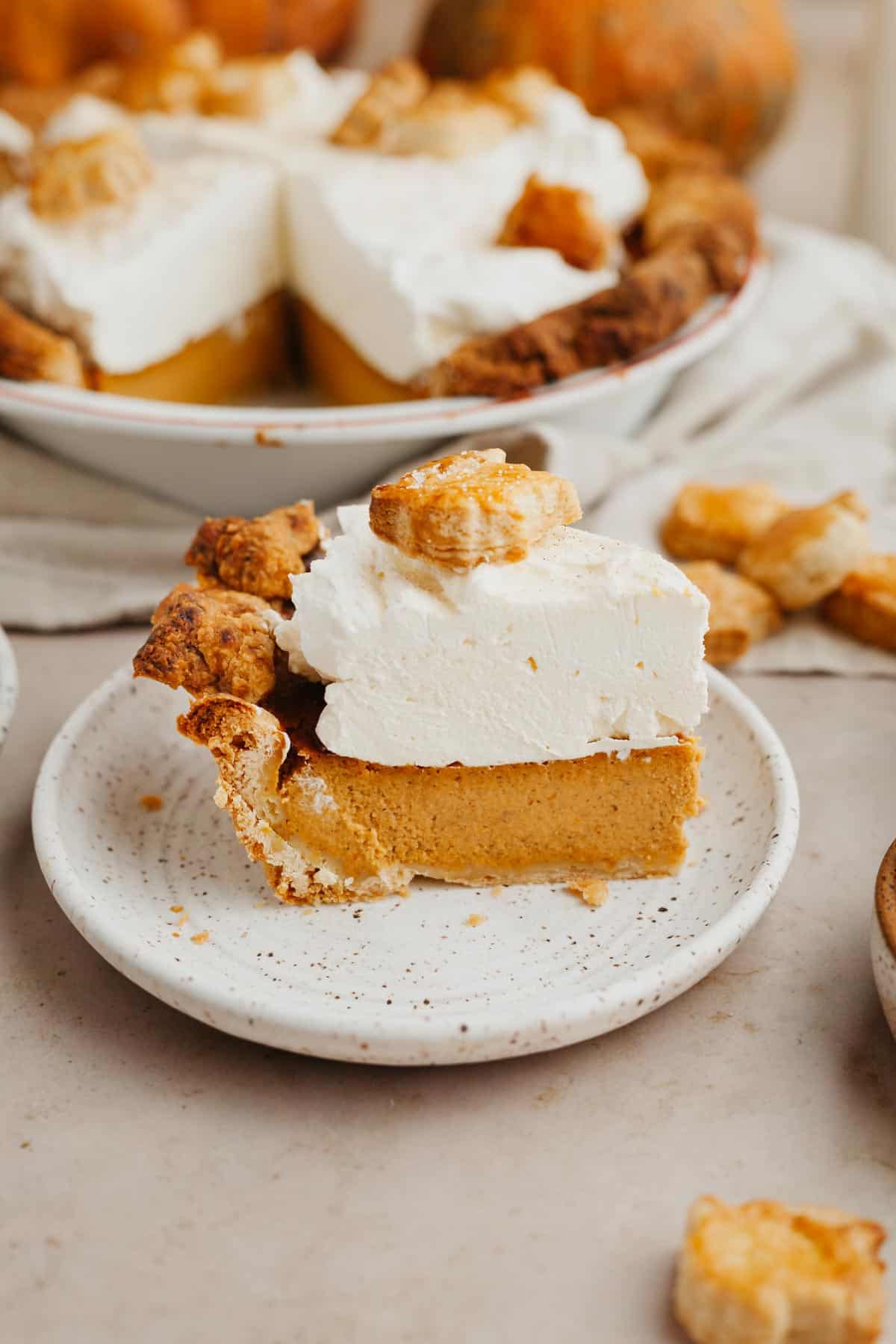 a slice of pumpkin pie on a small plate, the pie is covered in whipped cream.