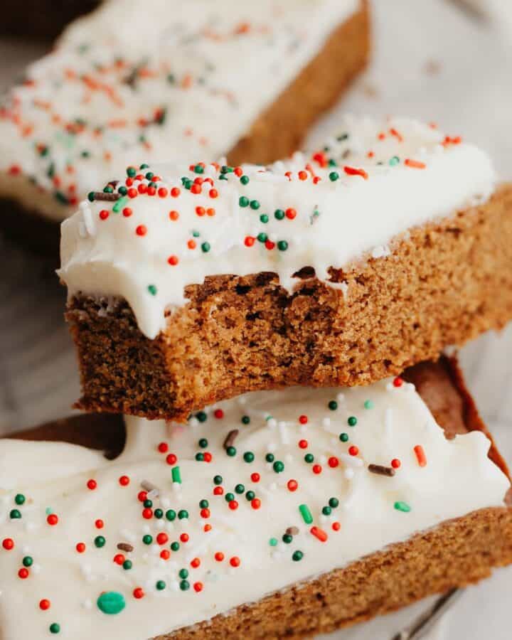 Three gingerbread cookie bars covered in cream cheese frosting, one has a bite taken out of it.
