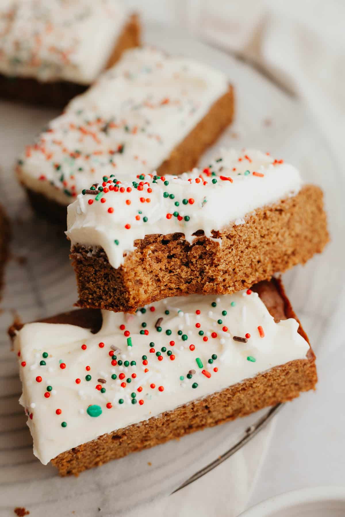 Three gingerbread cookie bars covered in cream cheese frosting, one has a bite taken out of it.