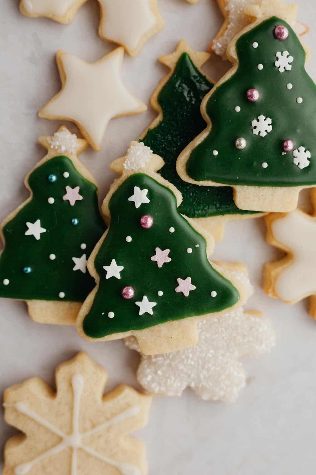 A small pile of cut out sugar cookies in the shape of Christmas trees.