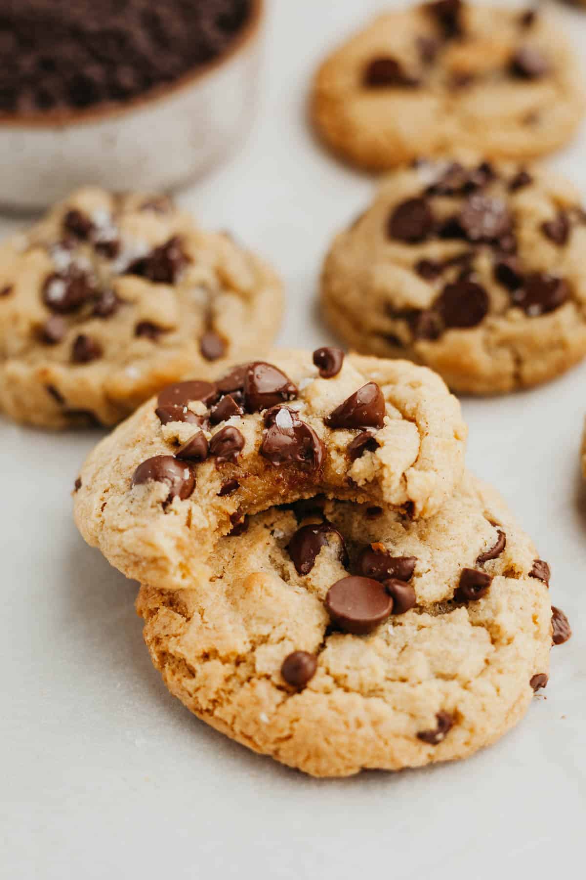 Chocolate chip cookies on parchment paper, one has a bite taken out of it.