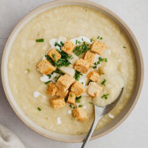 A bowl of cauliflower leek and potato soup with croutons and chopped dill.