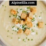A bowl of leek cauliflower and potato soup with croutons and chopped dill.
