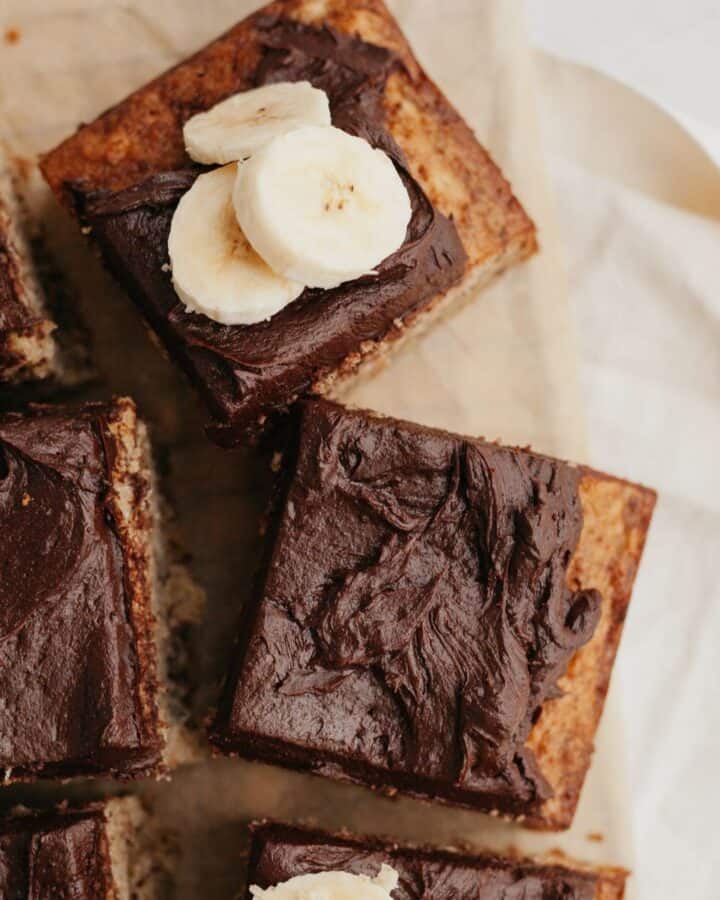 Squares of banana cake with chocolate frosting on parchment paper.
