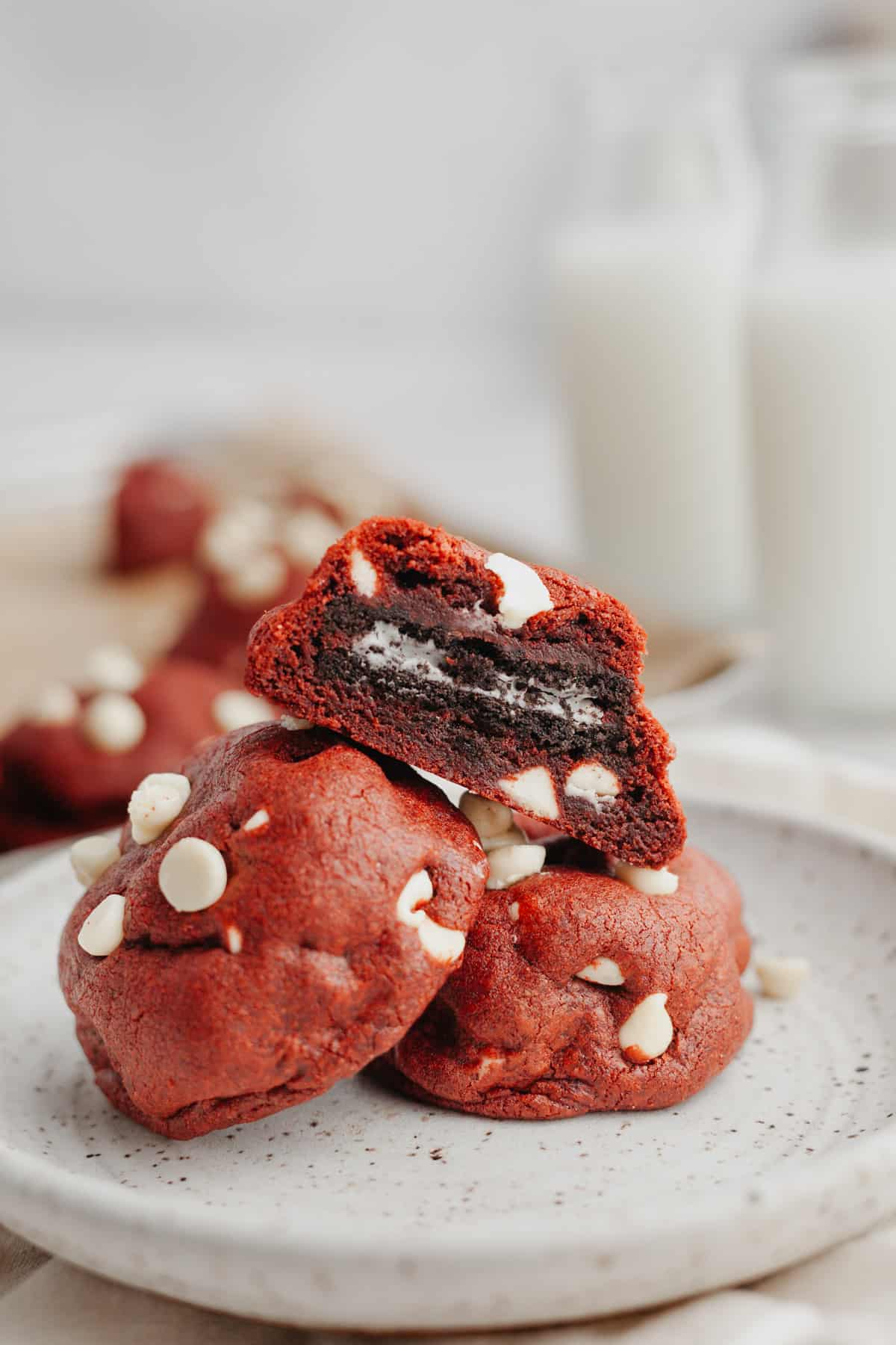 Three red velvet cookies on a plate, one is cut in half showing it is stuffed with an Oreo.