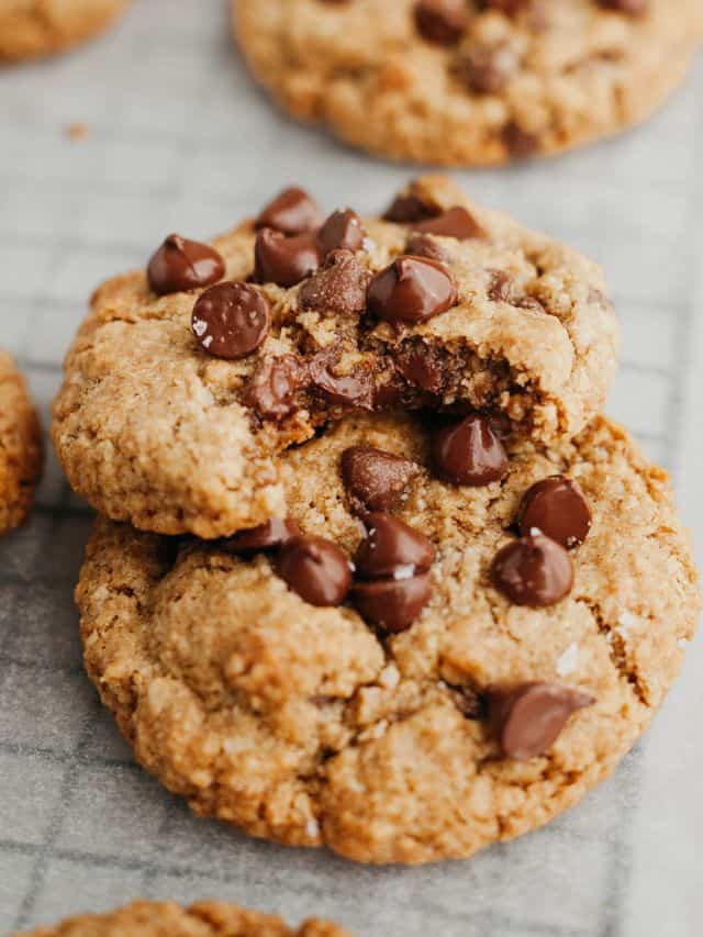Two chocolate chip oatmeal cookies on parchment paper, one has a bite taken out of it.