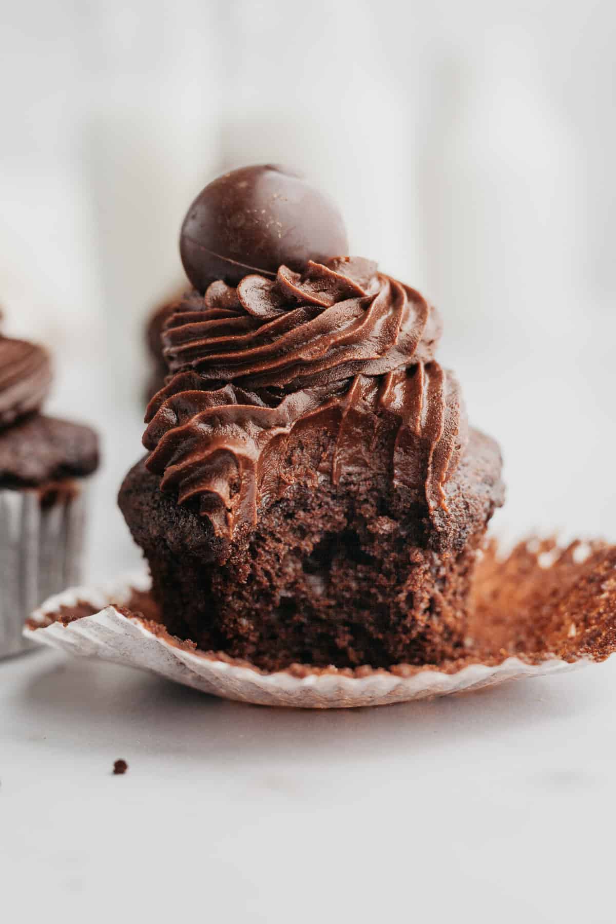 A close up of a chocolate fudge cupcake with a bite taken out of it.