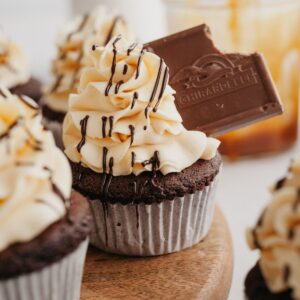 A chocolate cupcake with beige frosting, it has been topped with a chocolate caramel.