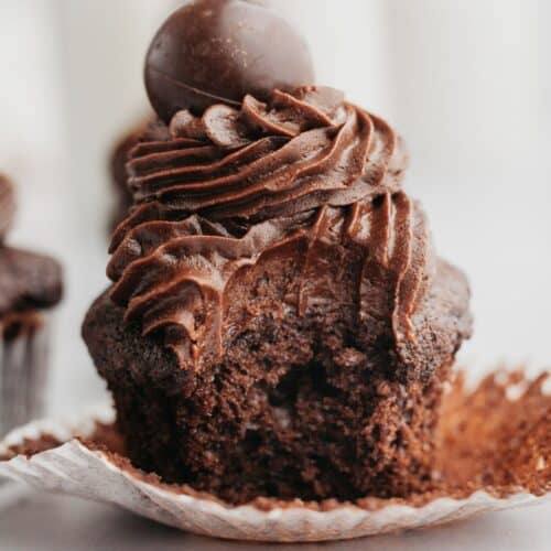 A close up of a chocolate fudge cupcake with a bite taken out of it.