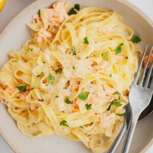 A bowl full of pasta with chopped parsley and salmon.