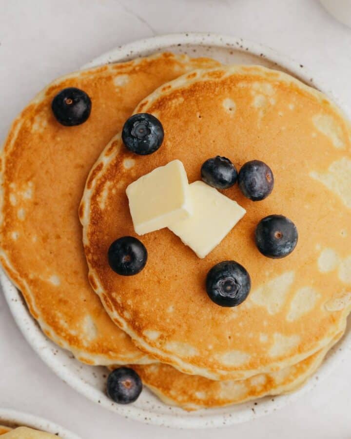 A small plate with three pancakes and blueberries.