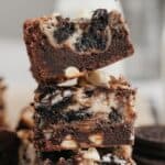 A stack of three Oreo cheesecake brownies on parchment paper.