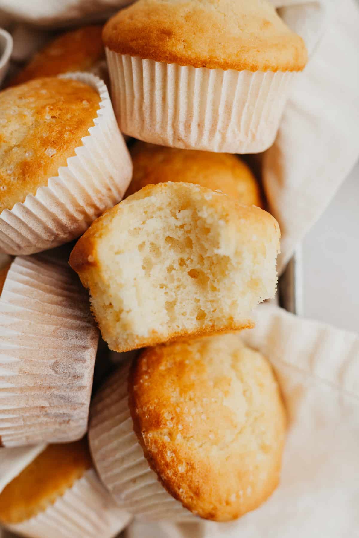 A small pile of vanilla muffins, one has a bite taken out of it.