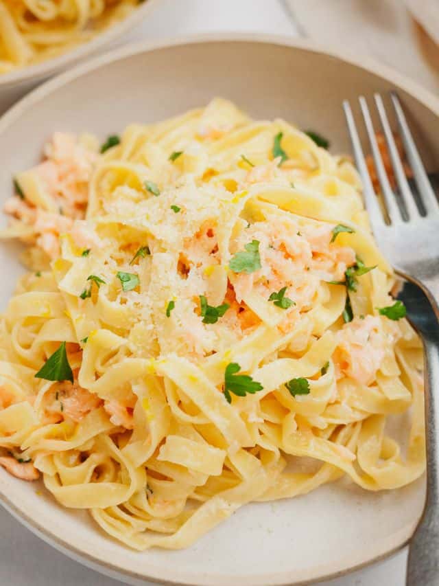 A bowl full of pasta with chopped parsley and salmon.