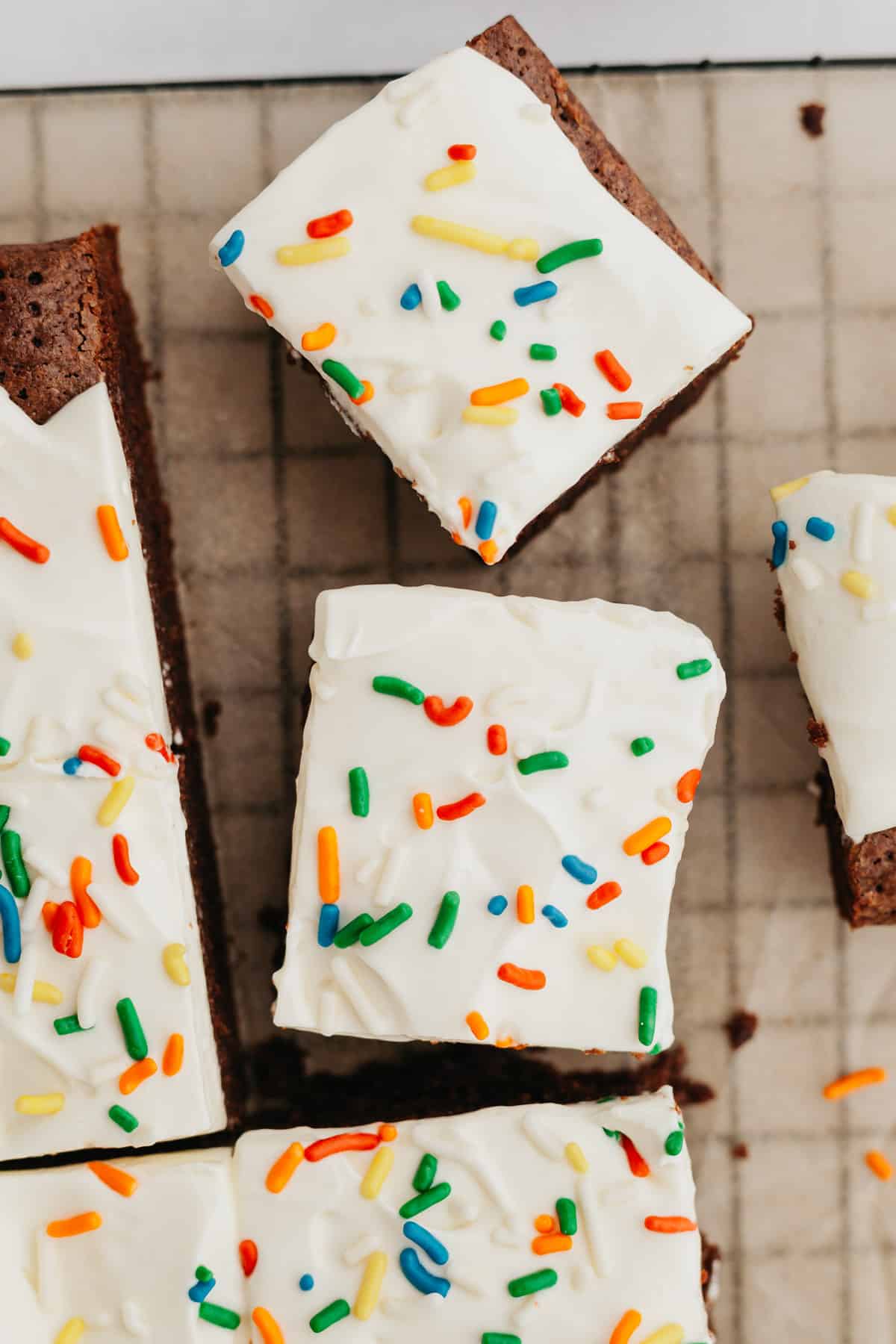 An overhead shot of brownies covered in cream cheese frosting and rainbow sprinkles.