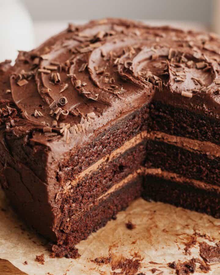 A triple chocolate layer cake on parchment paper, several slices have been taken out.