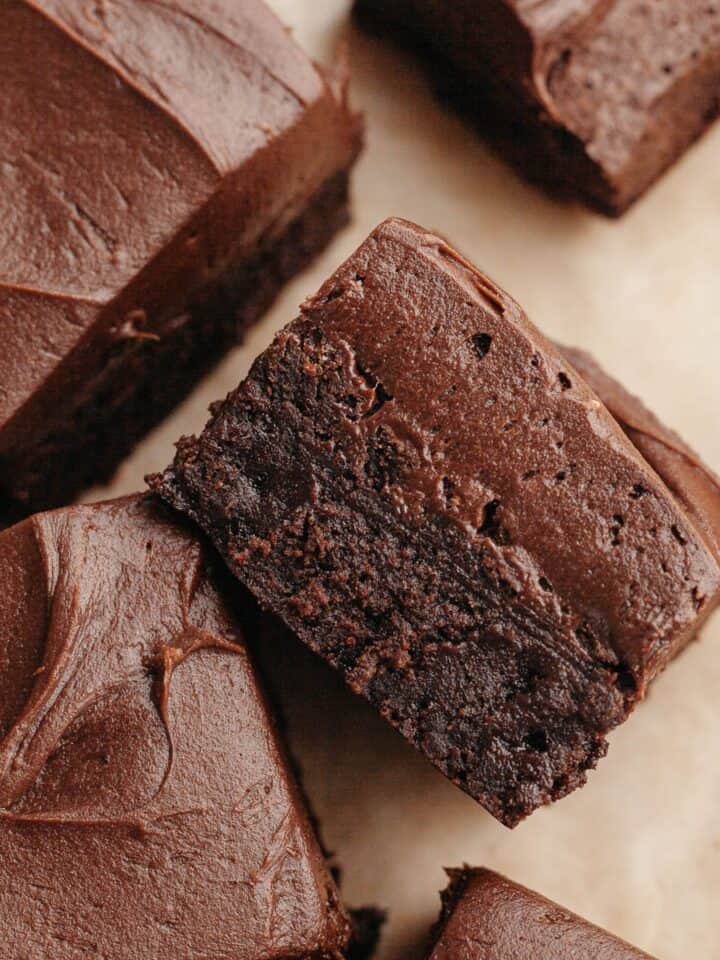Brownies covered in chocolate cream cheese frosting on parchment paper.