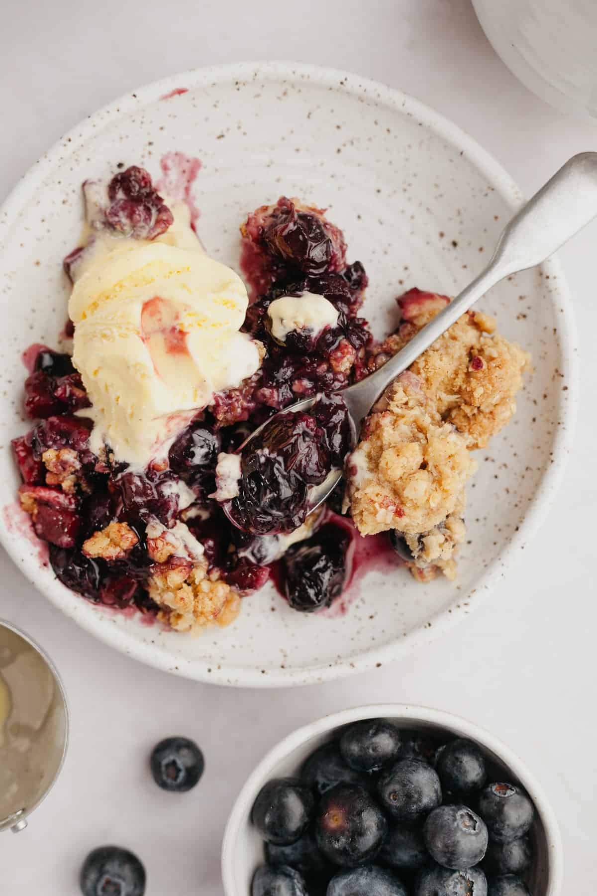 apple and blueberry crisp on a small plate with a scoop of ice cream.