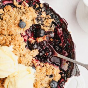 A blueberry apple crumble with two scoops of ice cream on top and a spoon.