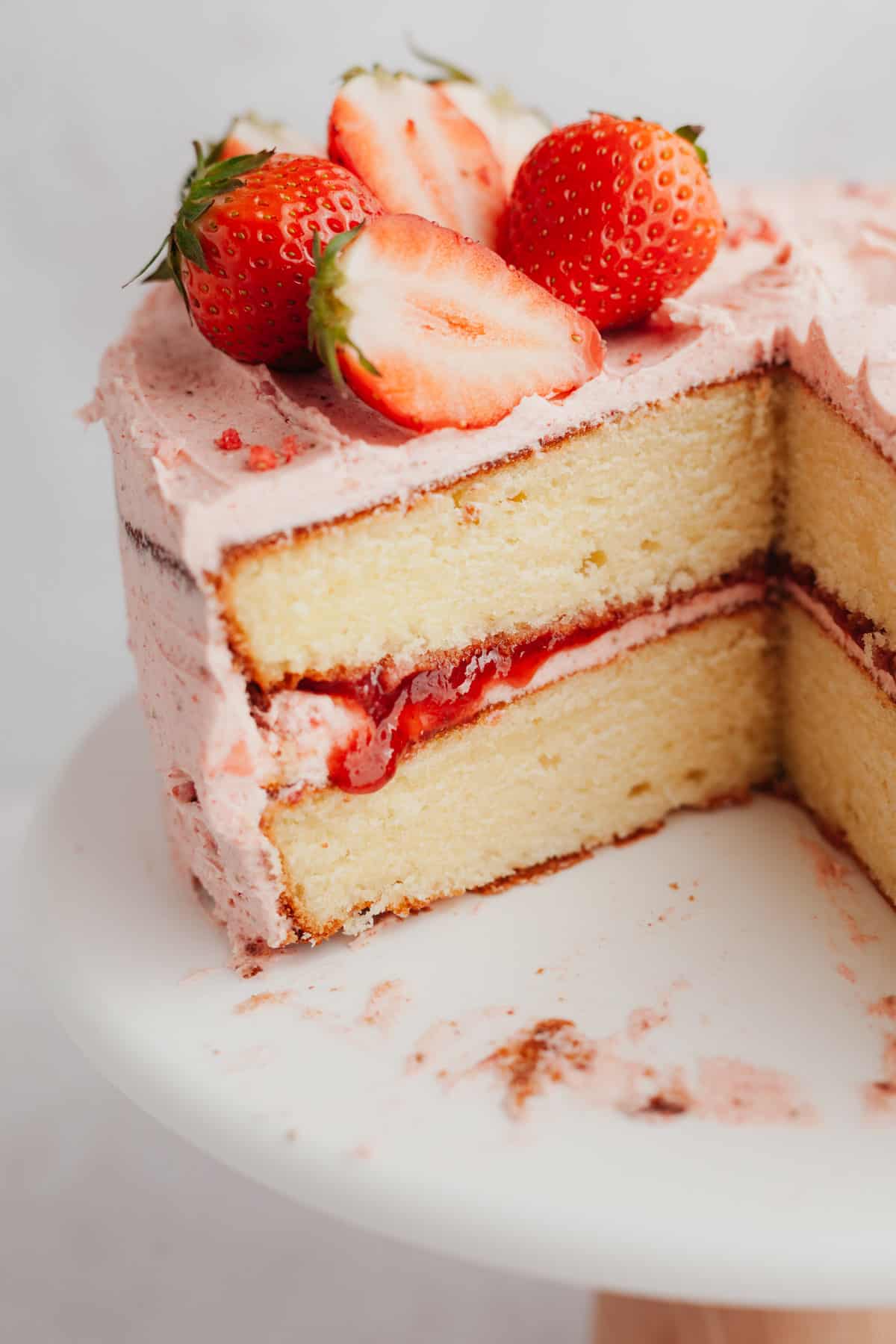 A close up of a two layer vanilla cake with a strawberry frosting, the cake has been cut.