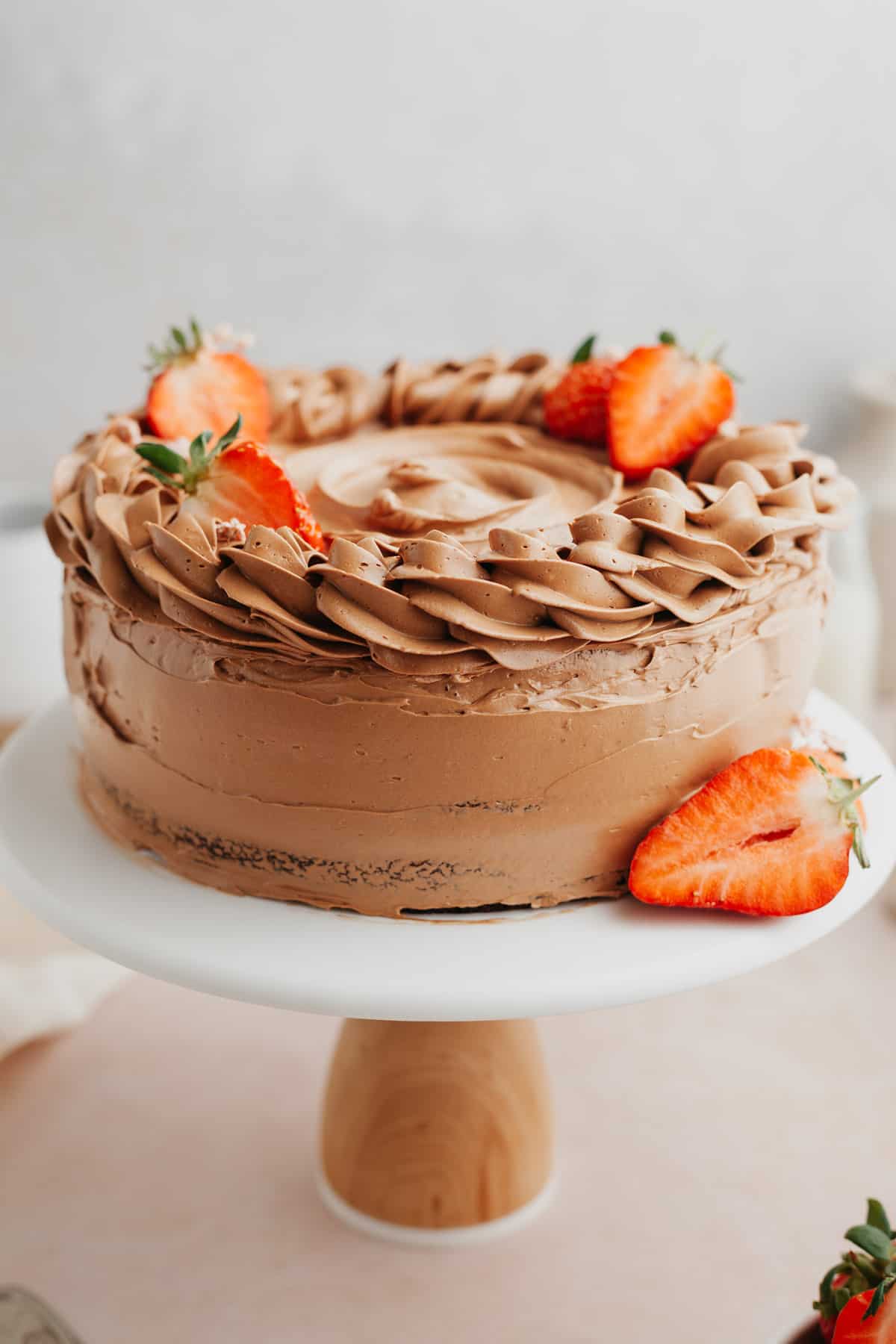 A chocolate cake decorated with strawberries on a white cake stand.