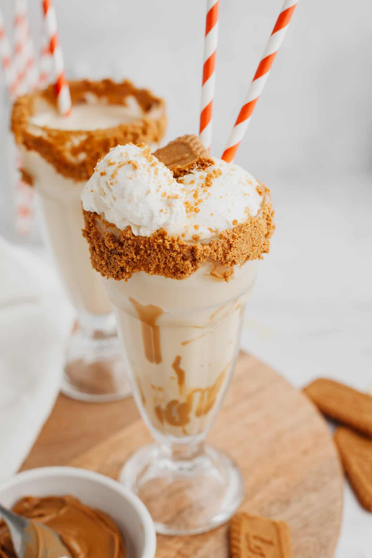 Two biscoff milkshakes in large glasses with red and white straws.
