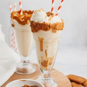 Two biscoff milkshakes in large glasses with red and white straws.