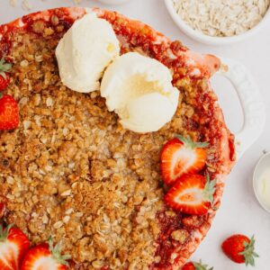 strawberry crumble in a white dish with sliced strawberries and two scoops of ice cream.