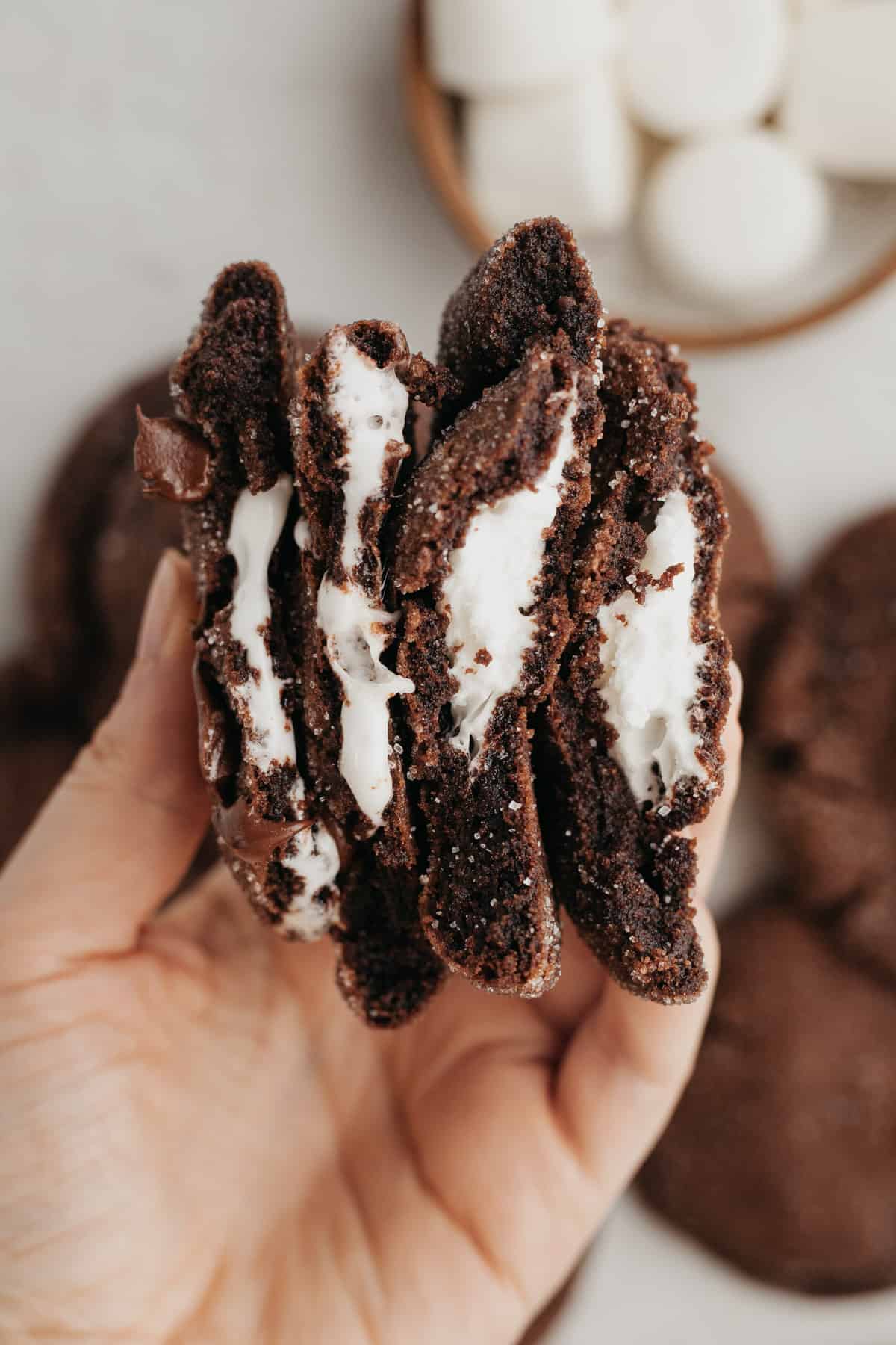 A hand holding four halves of chocolate marshmallow cookies.