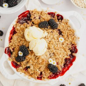 A blackberry apple crisp in a white dish with two scoops of ice cream on top.