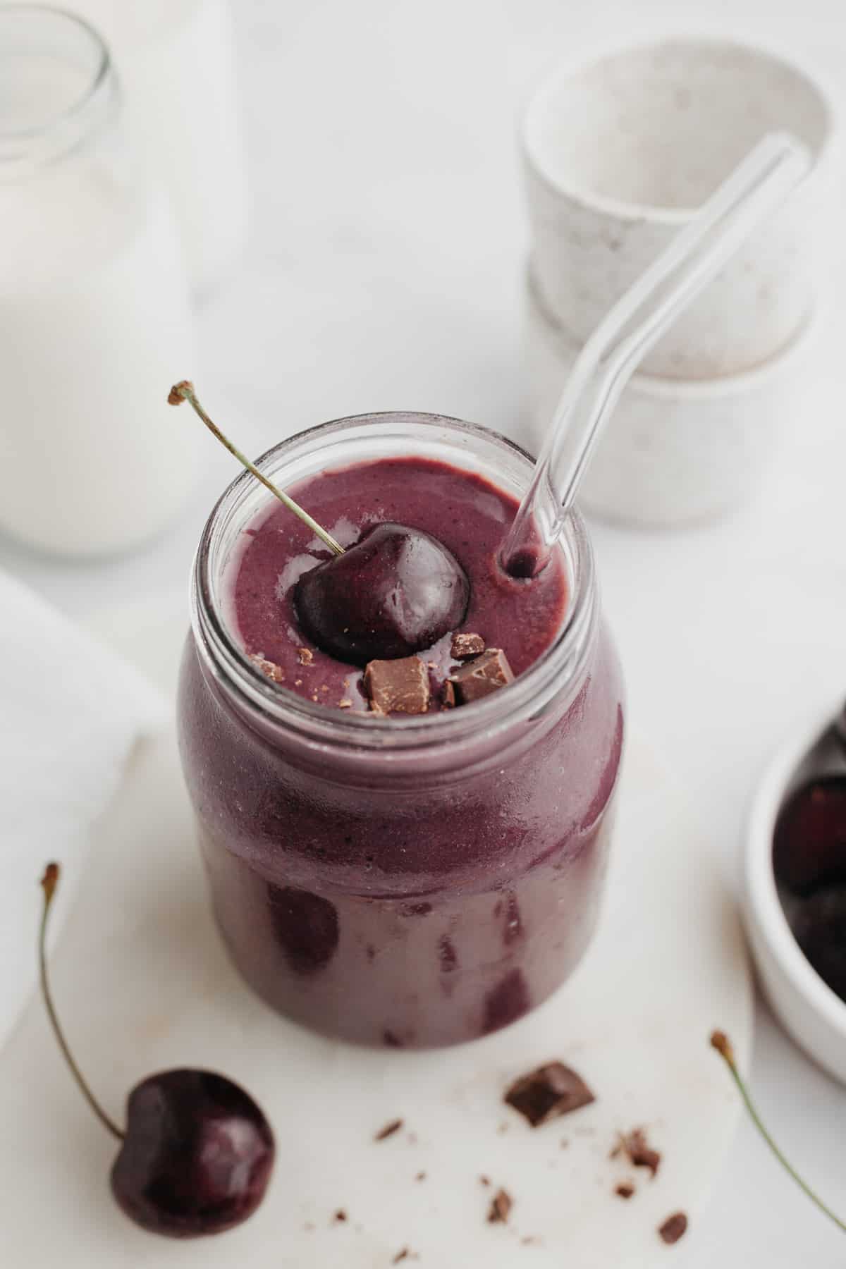 A chocolate cherry smoothie in a glass jar, it is topped with a fresh cherry.