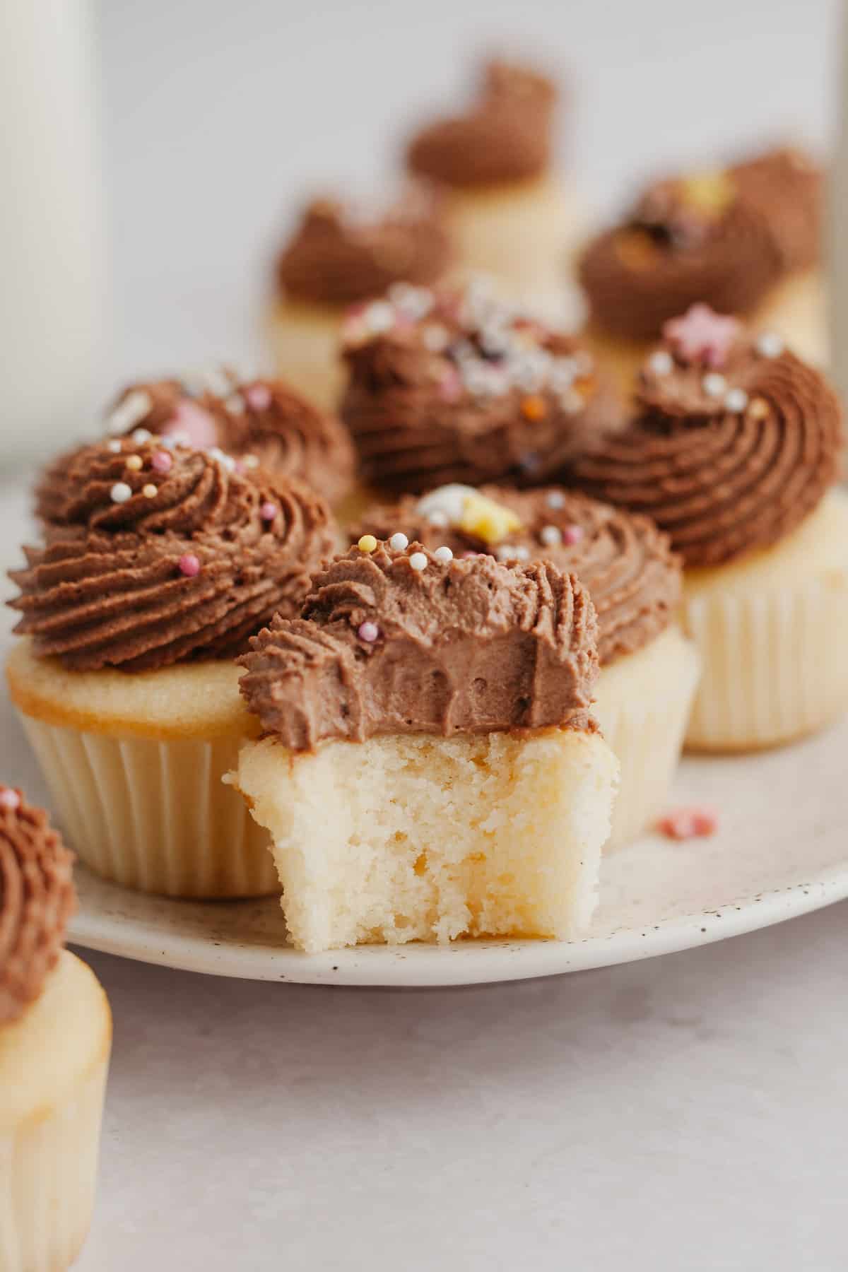 A close up of a mini vanilla cupcake with chocolate frosting, a bite has been taken out of it.