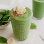 A large glass with a green smoothie in it, it is topped with banana slices.