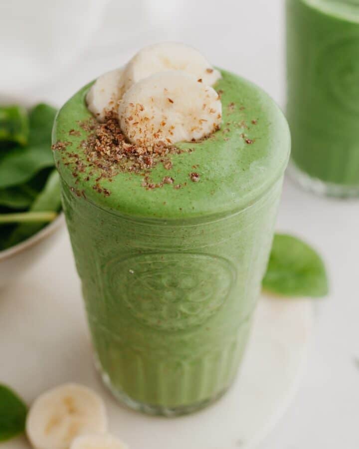 A large glass with a green smoothie in it, it is topped with banana slices.