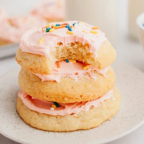 A stack of three Lofthouse style sugar cookies with pink frosting.