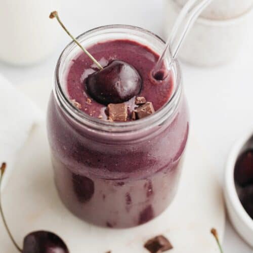A chocolate cherry smoothie in a glass jar, it is topped with a fresh cherry.