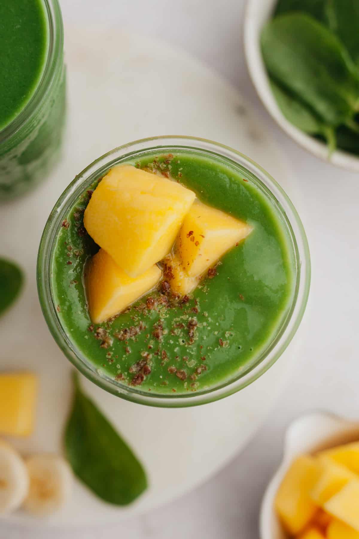 An overhead shot of a green smoothie with mango pieces.