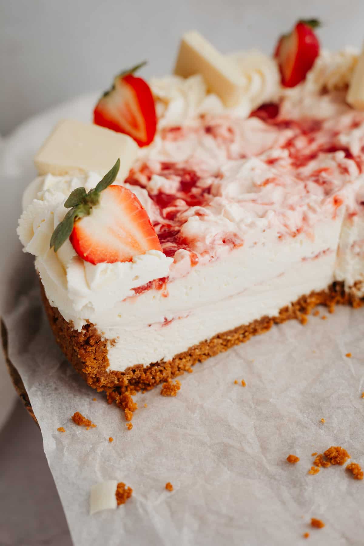 A slice of a strawberry white chocolate cheesecake on parchment paper.