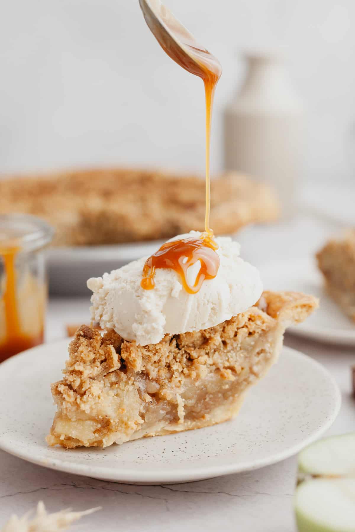 A slice of apple pie with a big scoop of vanilla ice cream on top and caramel sauce.