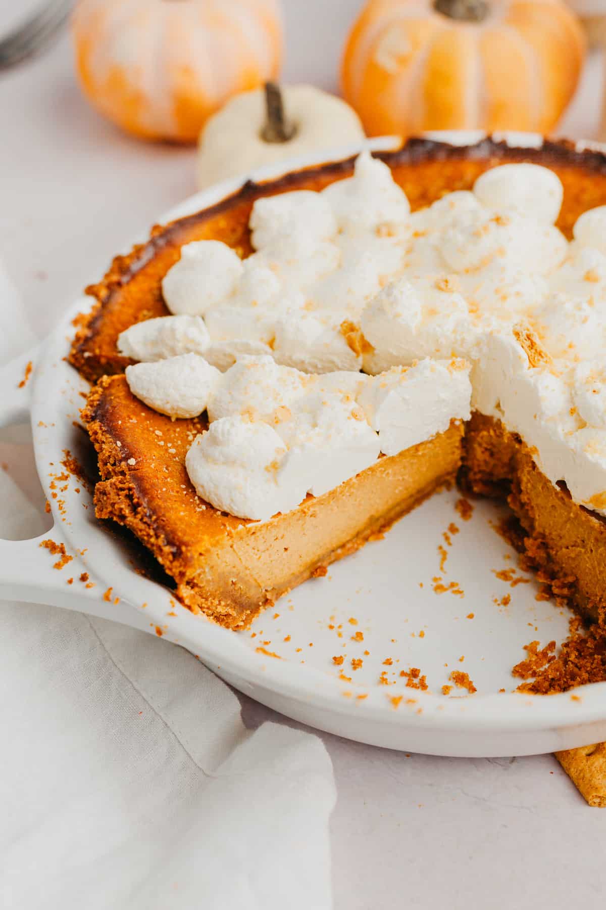 A pumpkin pie with graham cracker crust and topped with whipped cream.