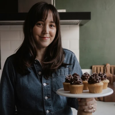 Ella from Alpine Ella is holding a cake stand with cupcakes on it.